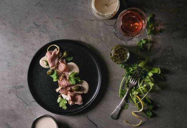 Veal with tuna sauce vitello tonnato Vitello tonnato italian dish. Thin sliced veal with tuna sauce, capers and coriander served on black plate, glass of rose wine and ingredients above over gray texture kitchen table. Top view, space tonatiuh stock pictures, royalty-free photos & images