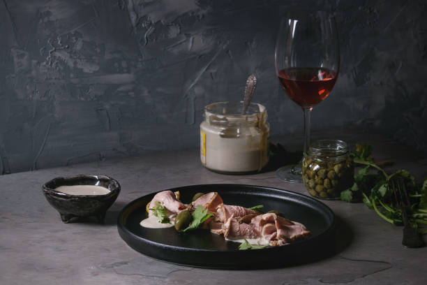 Veal with tuna sauce vitello tonnato Vitello tonnato italian dish. Thin sliced veal with tuna sauce, capers and coriander served on black plate, glass of rose wine and ingredients above over gray texture kitchen table. tonatiuh stock pictures, royalty-free photos & images