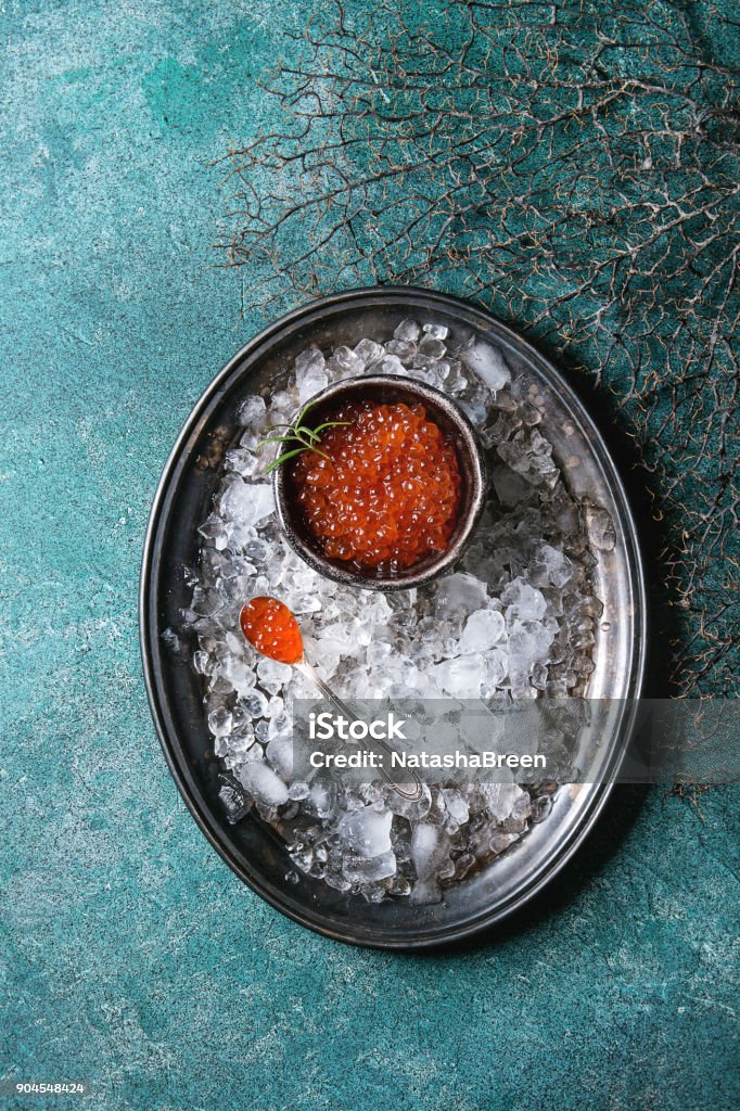 Bowl of red caviar Bowl of red caviar on vintage metal tray with ice over turquoise texture background. Top view, space Fish Stock Photo