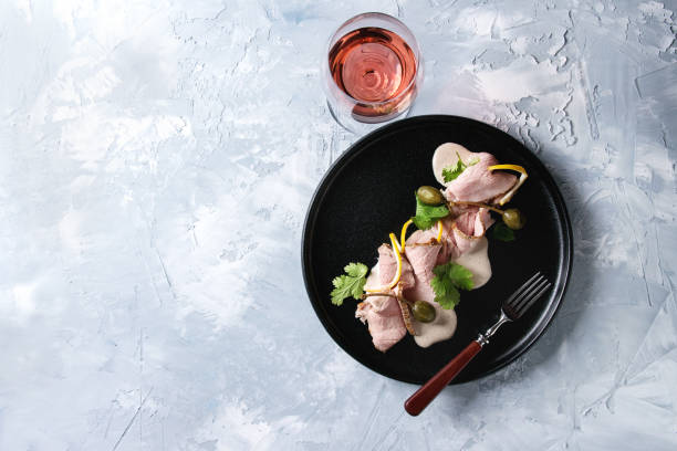 Veal with tuna sauce vitello tonnato Vitello tonnato italian dish. Thin sliced veal with tuna sauce, capers and coriander served on black plate with fork and glass of rose wine over gray texture background. Top view, space tonatiuh stock pictures, royalty-free photos & images