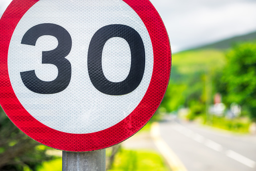 Close-up of a speed limit sign for 30 miles per hour on a narrow road through a British village.