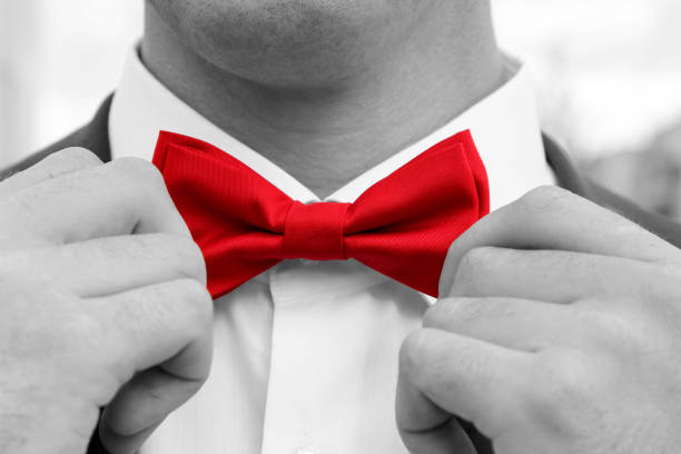 Man adjusts red bow tie with hands. Black and white photo with coloured element