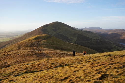 Pentland Hills, Edinburgh, Scotland - December 03 2017: Two hikers in the Pentland Hills, Edinburgh making their way from the top of Turnhouse Hill, from where the shot was taken, towards Carnethy Hill. The low angle of the December mid-day sun catches only one side of the hill range.