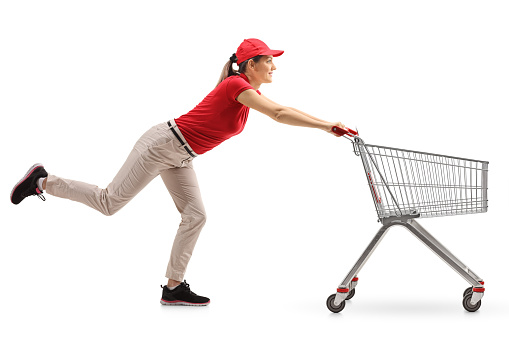 Full length profile shot of a delivery girl pushing an empty shopping cart isolated on white background