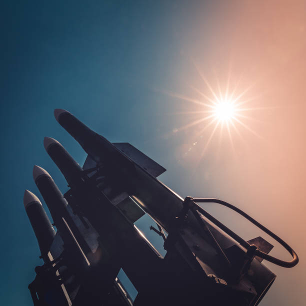 Four rockets of anti-aircraft missile system are directed upwards against the background of blue sky and sun at sunset stock photo