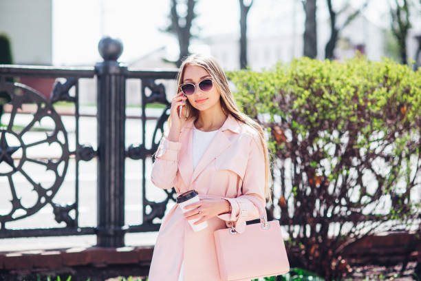 upper class woman. fashionable woman texting outdoors. fashion woman in a sunglasses and pink jacket with coffee - upper class women wealth fashion model imagens e fotografias de stock