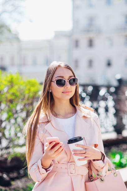 upper class woman . fashionable woman texting outdoors. fashion woman in a sunglasses and pink jacket with coffee - upper class women wealth fashion model imagens e fotografias de stock