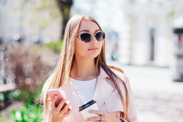 upper class woman . fashionable woman texting outdoors. fashion woman in a sunglasses and pink jacket with coffee - upper class women wealth fashion model imagens e fotografias de stock