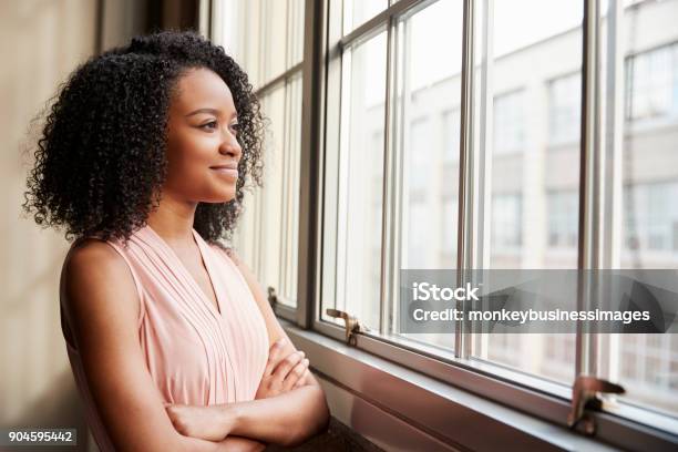 Joven Negro Mujer Con Los Brazos Cruzados Mirando Por La Ventana Foto de stock y más banco de imágenes de Mirar por la ventana