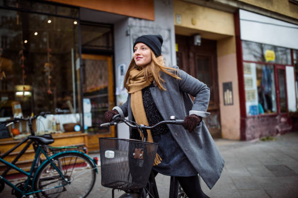 Smiling young woman riding bicycle by building Smiling young woman riding bicycle. Female is cycling on street by building. She is in warm clothing at city. winter city stock pictures, royalty-free photos & images