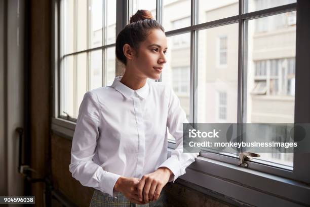 Young Woman With Hair Bun Looking Out Of Window Waist Up Stock Photo - Download Image Now