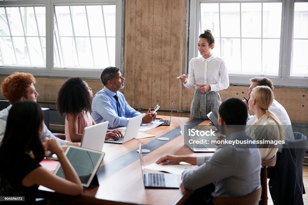 Female manager stands addressing team at board meeting Leadership Stock Photo