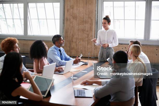 Female Manager Stands Addressing Team At Board Meeting Stock Photo - Download Image Now
