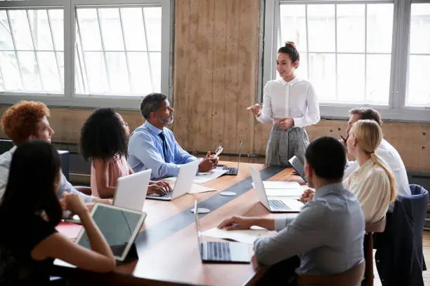 Photo of Female manager stands addressing team at board meeting