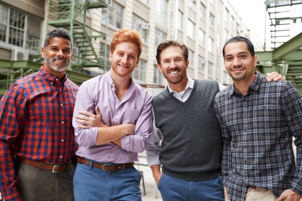 quatre collègues masculins, souriant à la caméra à l’extérieur - seulement des hommes photos et images de collection