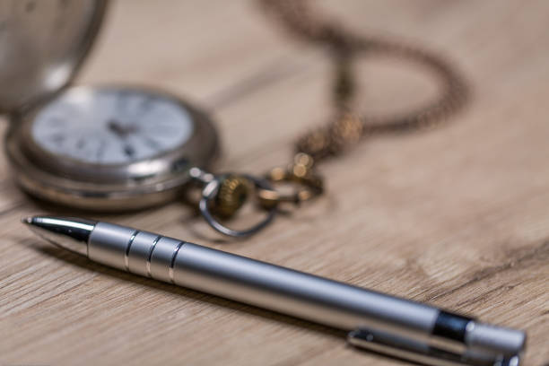 istock Pen and old silver pocket watch on wooden table 904620884