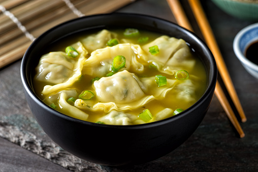 A bowl of delicious chinese wonton soup with green onion garnish.