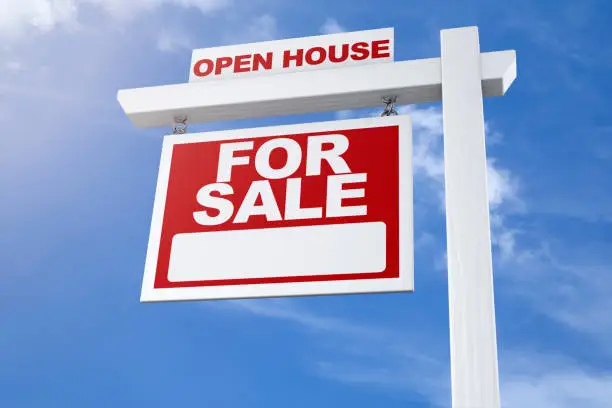 A realtors open house real estate for sale sign against a blue summer sky from a low angle with no people.