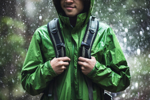 junger mann wandern im regen mit wasserdichte jacke - wasserdicht stock-fotos und bilder