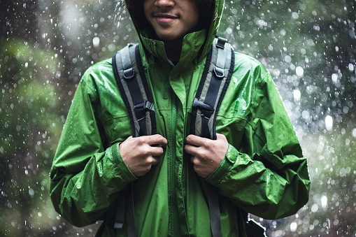 A cheerful young adult African American man goes for a hike in the rain in the Pacific Northwest, the raindrops repelling from his raincoat.  Shot in Washington state.