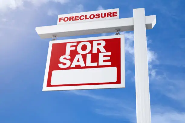 A realtors foreclosure real estate for sale sign against a blue summer sky from a low angle with no people.