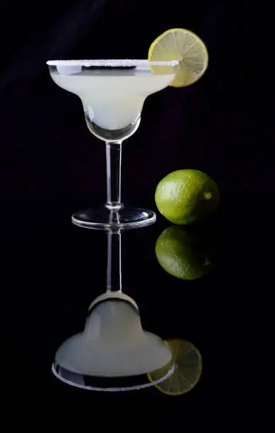 Margarita cocktail and lime on black background.