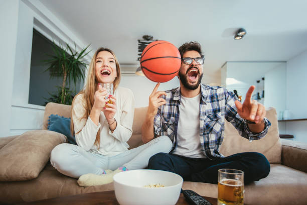 istock Couple watching tv in living room while eating popcorn and drinking beer 904697290