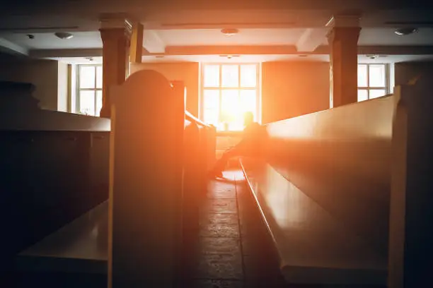 Photo of Silhouette of man praying in church in sunset light