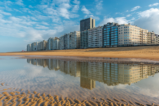 The skyline of Ostend City with its waterfront promenade reflecting in the North Sea with sand patterns at sunset, West Flanders, Belgium.