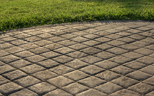 Stamped concrete pavement cobblestones pattern, decorative appearance colors and textures of paving cobblestones tile on cement flooring in a park with green lawn