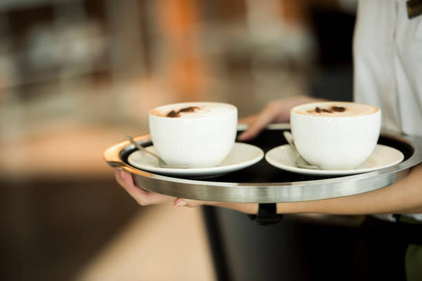 Waiter is serving two cups of coffee on a tray, selective focus