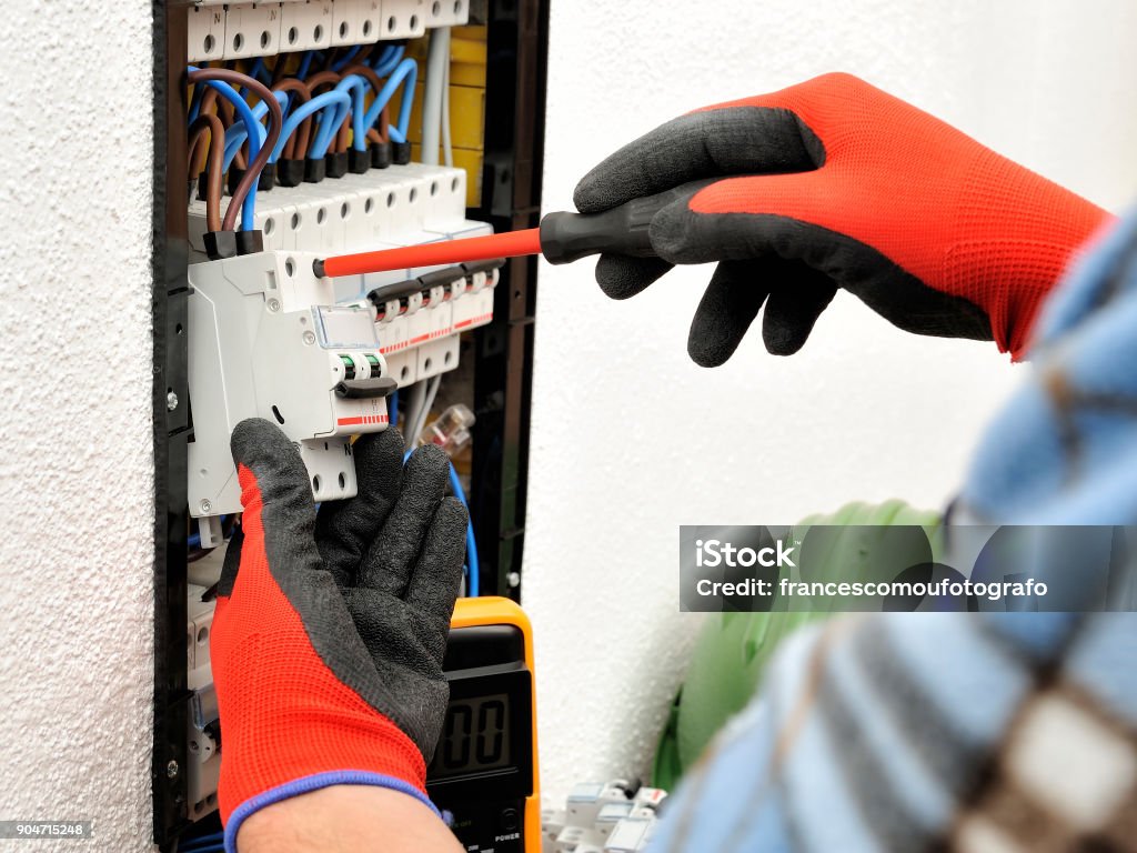 Young electrician technician at work on a electrical panel with protective gloves Young electrician technician fixes the electric cable to the magnetothermic switch with the screwdriver Adult Stock Photo