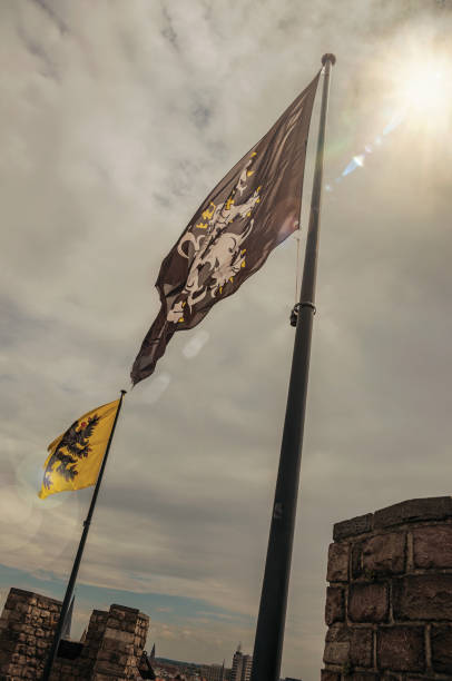 bandeiras e céu nublado na torre do castelo gravensteen em ghent. - flag flanders medieval lion - fotografias e filmes do acervo