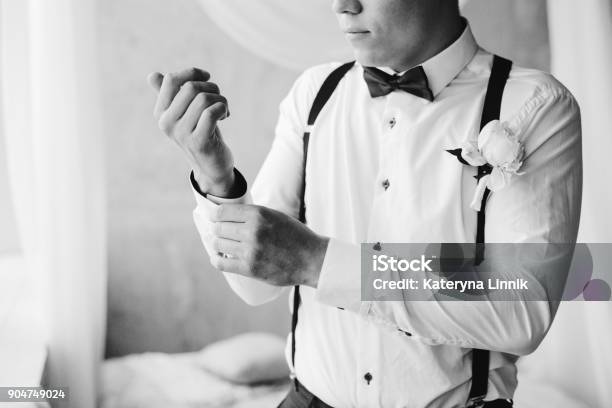 Grooms Morning Preparation Handsome Groom In Bow Tie Suspenders Getting Dressed And Preparing For The Wedding At Hotel The Bridegroom Wears Cufflinks In A White Shirt Black And White Portrait Stock Photo - Download Image Now