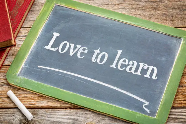 Love to learn - white chalk text on a slate blackboard with books