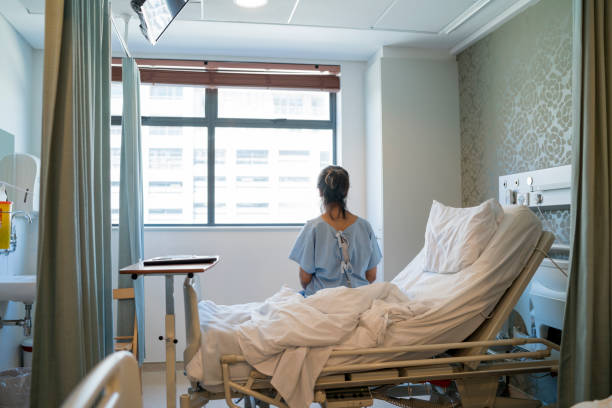 paciente femenino de sentado en cama en sala de hospital - examination gown fotografías e imágenes de stock