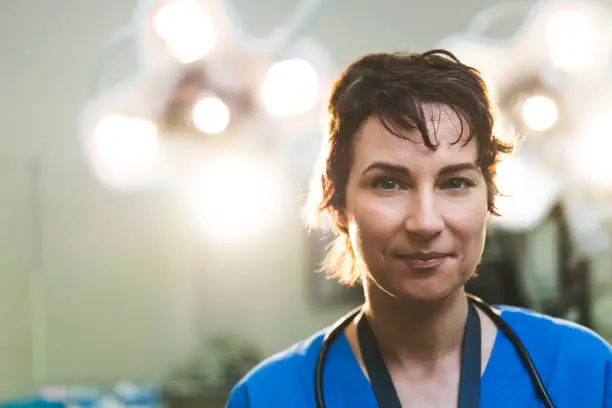 Portrait of smiling female doctor. Healthcare worker is against illuminated lights in hospital. She is having short hair.