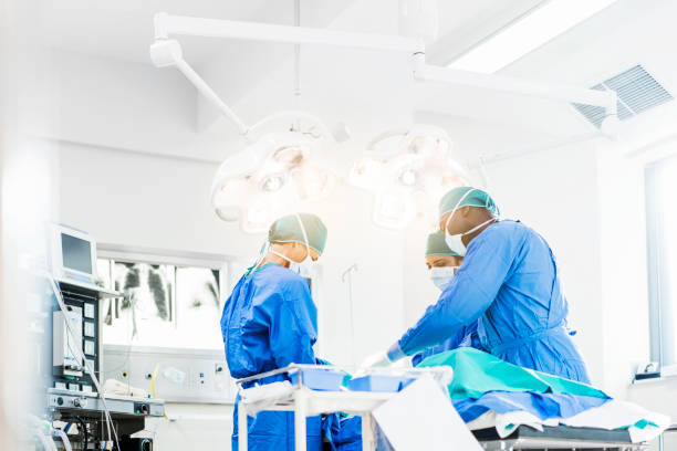 Surgeons operating below lighting equipment Surgeons operating below lighting equipment. Male and female doctors are wearing blue scrubs. They are working in hospital. operating room photos stock pictures, royalty-free photos & images