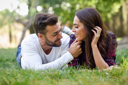 Young girl is resting on her boyfriend's lap, who's sitting on the grass