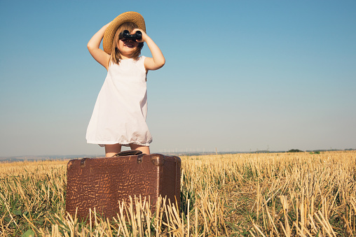 Little girl with suitcase is looking trough binoculars