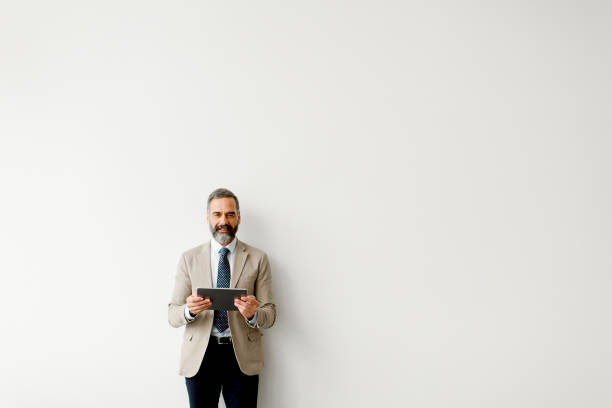 istock Handsome senior businessman with tablet by wall 904827070