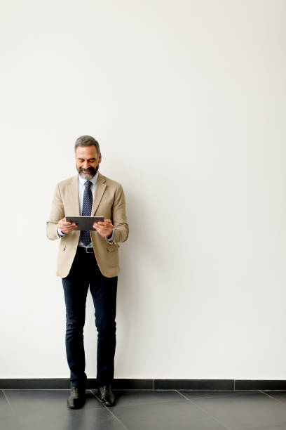 istock Handsome senior businessman with tablet by wall 904827080