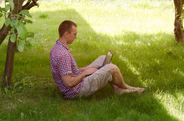 istock Man working on laptop on the grass in garden. Side view 904832460