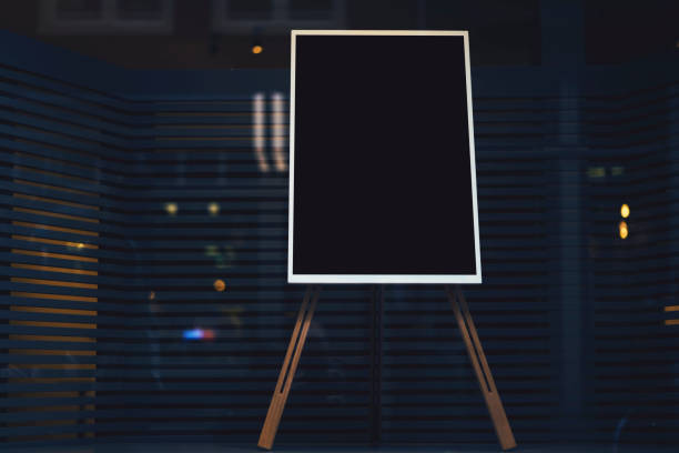 istock Black stylish chalkboard with mock up copy space are for your text message or advertising promotional content, empty presentation wooden board standing on the glass storefront 904833184