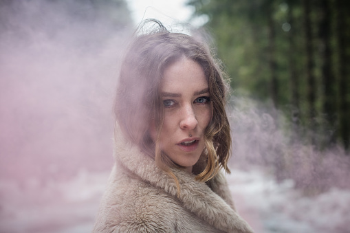 Young woman portrait outdoors in the woods with smoke bombs; Europe.