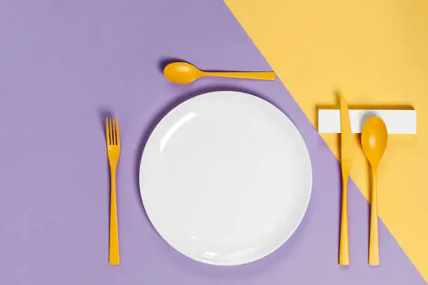White utensils and yellow cutlery on a pastel colored background. Colors in the style of pop.