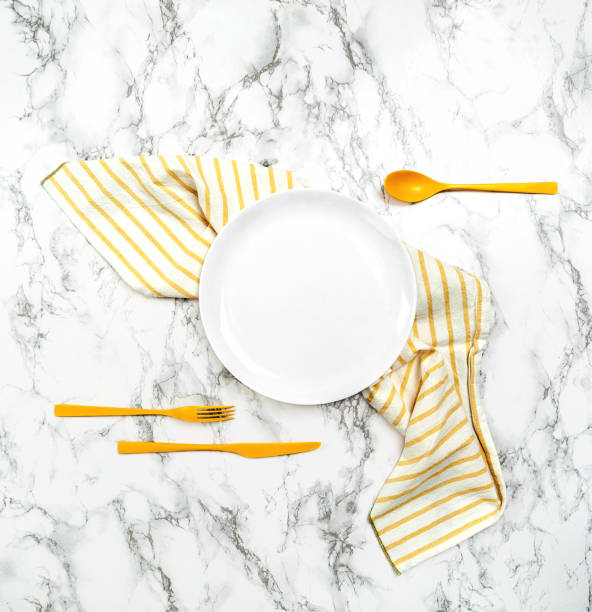 White dish, striped napkin and yellow cutlery on the marble table. stock photo