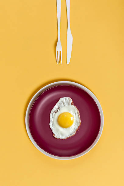 istock Fried egg on a burgundy plate on a yellow background. Breakfast in a minimalist style. 904834124