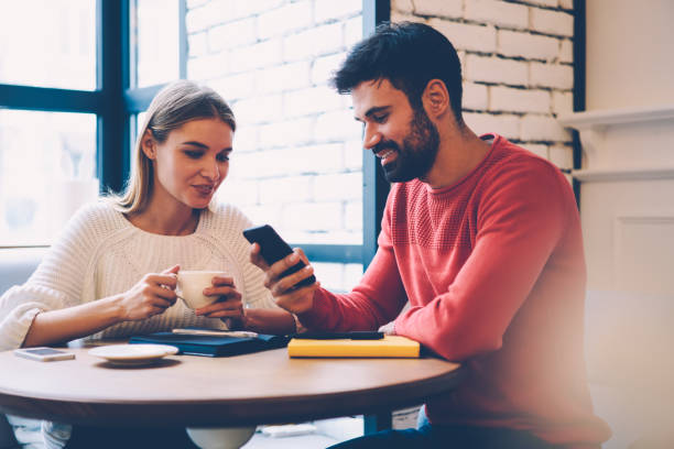 istock Smiling romantic couple watching video on smartphone while enjoying spending time together on coffee break, bearded guy showing photos on mobile to his pretty girlfriend communicating during date 904837514