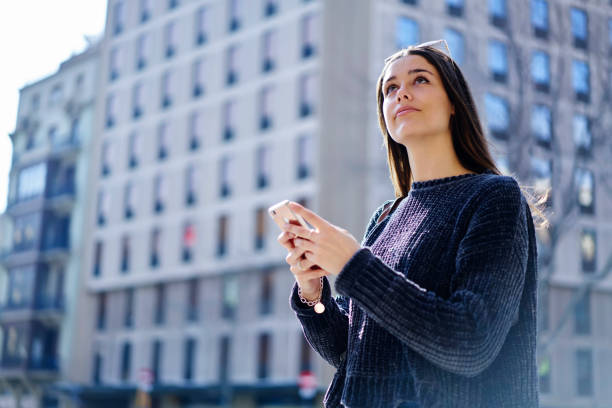 istock Charming tourist dressed in casual outfit using application on smartphone searching direction for walking in sightseeing tour looking up enjoying spring sunny day in town standing near advertising area 904838536